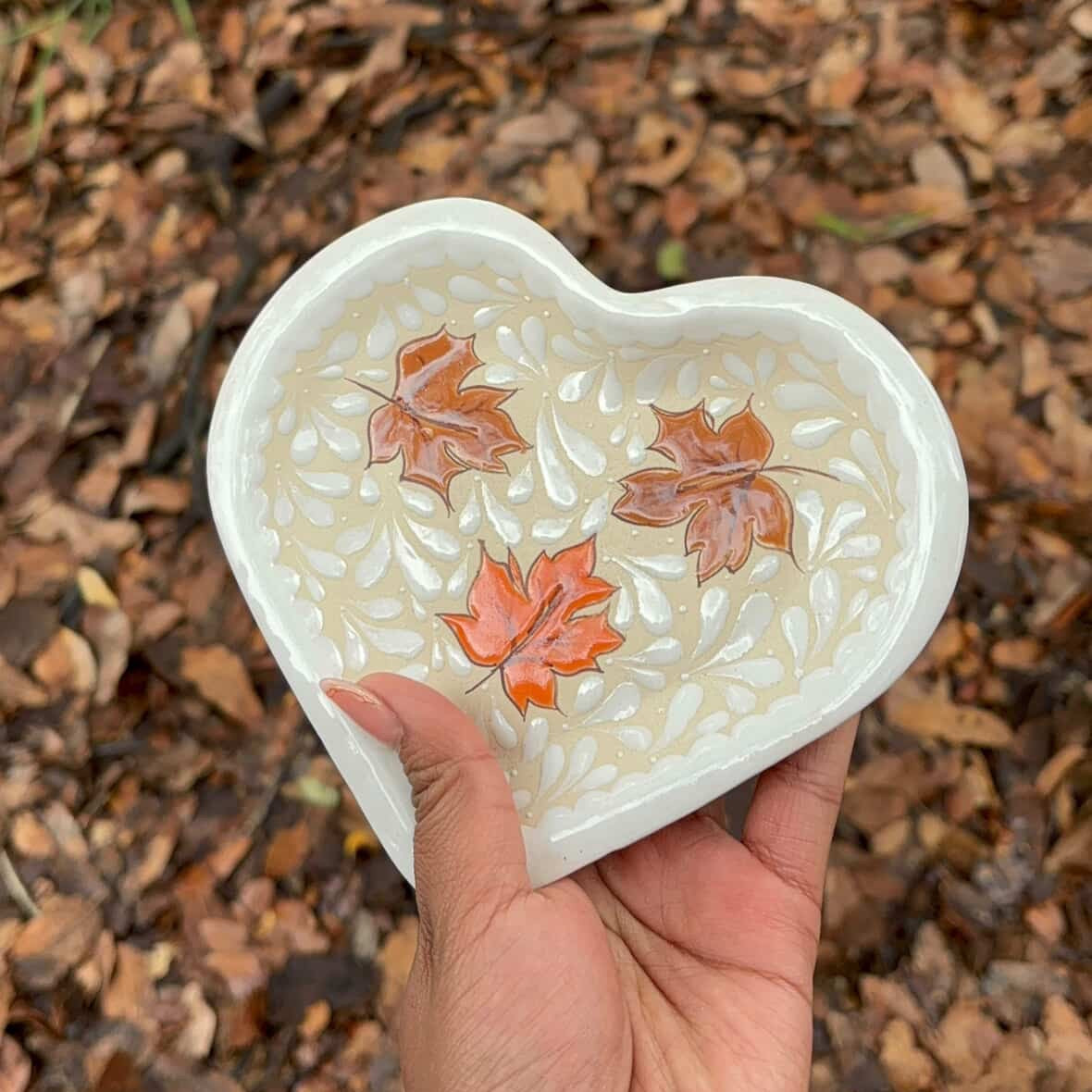 Heart-shaped dish with autumn leaves held over a leaf-covered ground